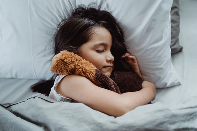 Child sleeping in bed with her teddy bear