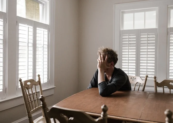 tired and stressed man sitting at a kitchen table with head in hands